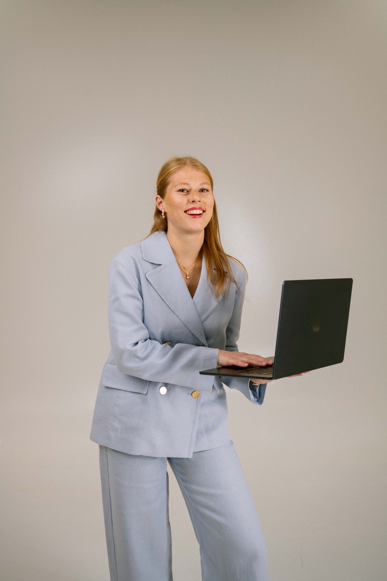 Kalu, founder of Weddings & Events with Kalu, smiling in a light blue suit and holding an open laptop in a bright studio.
