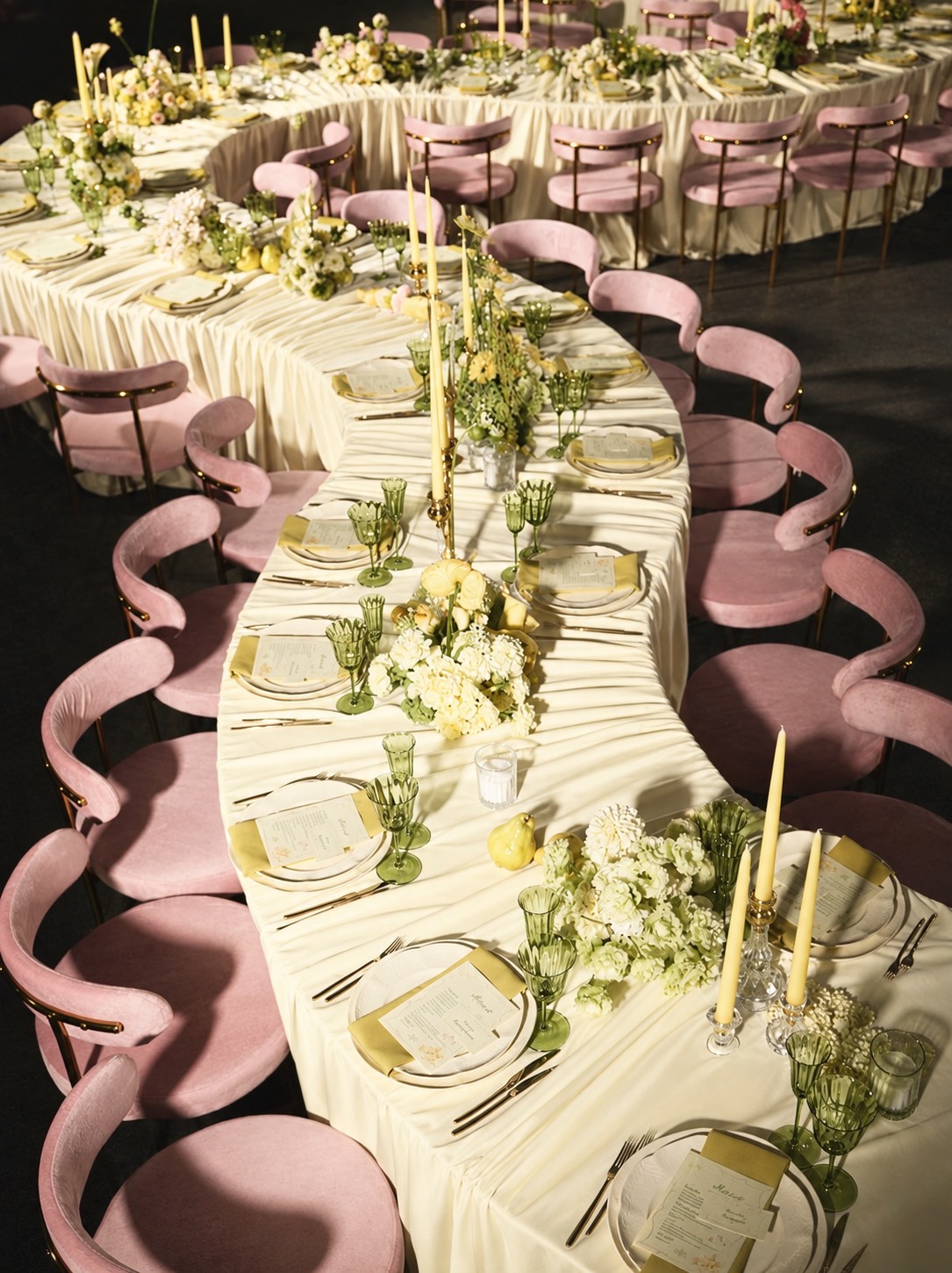 Long serpentine dinner table with pink velvet chairs and candles (AI-generated image)