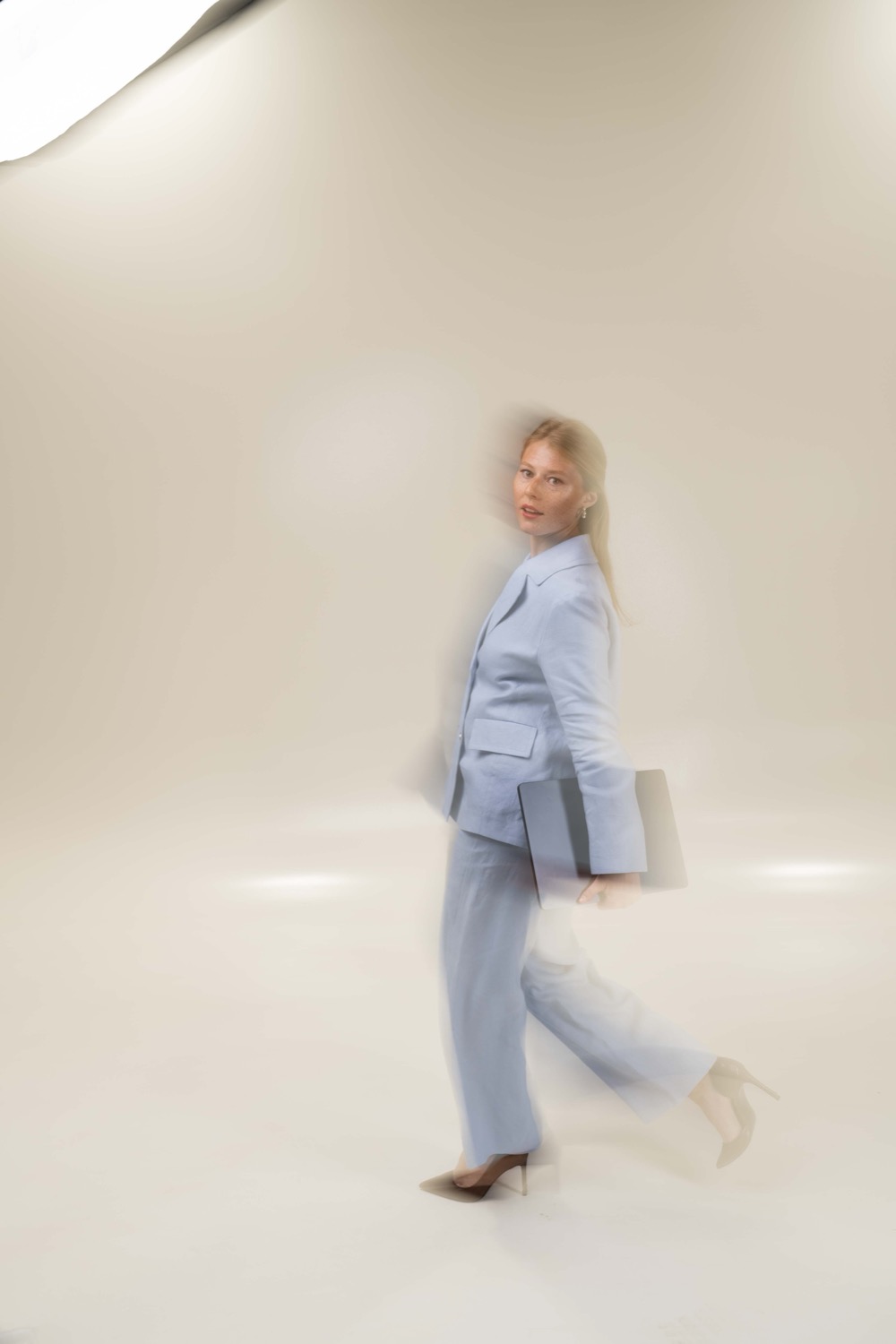 Kalu walking through a bright studio in a light blue suit, carrying a folder